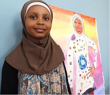 Girl in headscarf stands next self portrait, she looks confident and relaxed. 